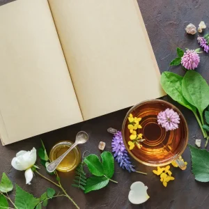 A dark background featuring an arrangement of flowers, tea, herbs, and an open book, creating a serene and cozy atmosphere